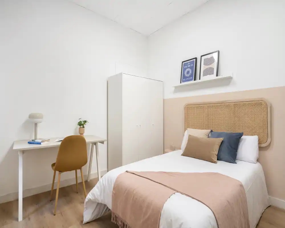 Dormitorio luminoso y elegante con cabecero de ratán, ropa de cama suave y un pequeño escritorio — ideal para estancias cómodas y teletrabajo.