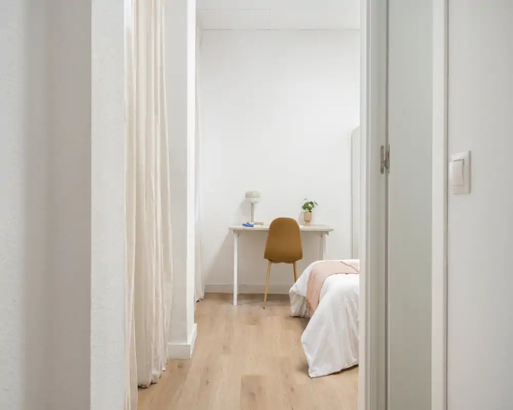 Dormitorio luminoso y minimalista con cama cómoda y un pequeño escritorio — estilo moderno y suelo de madera cálido.