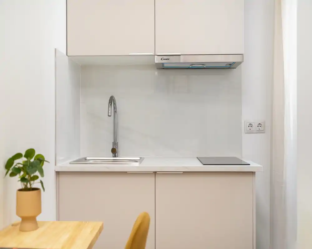 Cocina compacta y moderna con fregadero integrado, placa de inducción y mobiliario en tonos neutros; diseño luminoso y minimalista ideal para estudios.