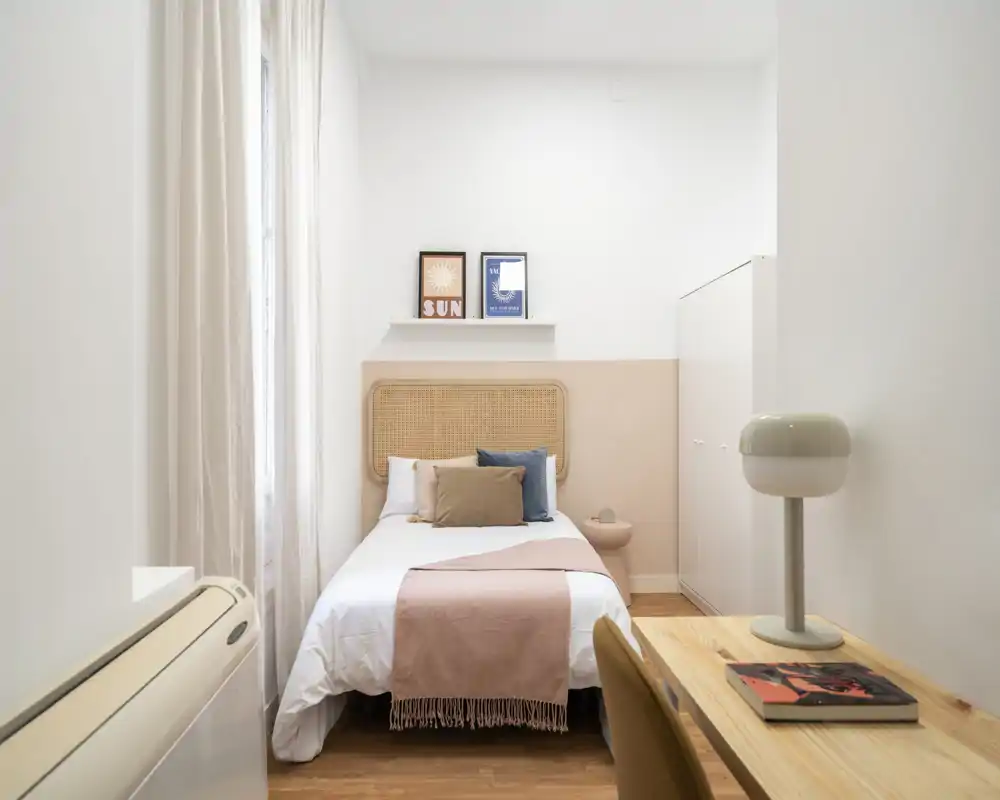 Dormitorio luminoso y minimalista con cama individual centrada, textiles neutros y suaves, pequeña mesita y armario — ideal para una habitación en alquiler acogedora y bien iluminada.