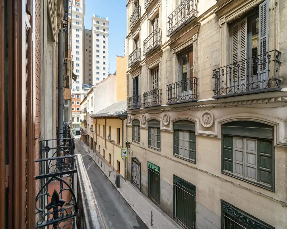 Vista soleggiata su una strada stretta dalla balconata, con facciate classiche e ringhiere in ferro battuto su una tranquilla via pedonale.