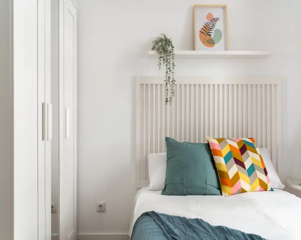 Dormitorio luminoso y moderno con cabecero de listones, cojines coloridos y textiles suaves que crean un ambiente acogedor.