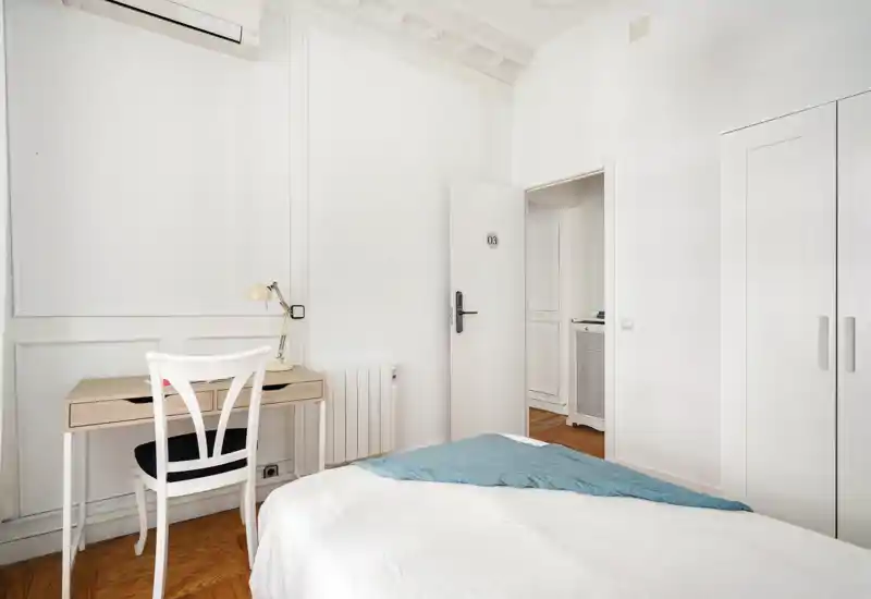 Camera da letto minimalista e luminosa con letto bianco, plaid azzurro e una scrivania in legno: ambienti puliti e soffitti alti che danno una sensazione ariosa.