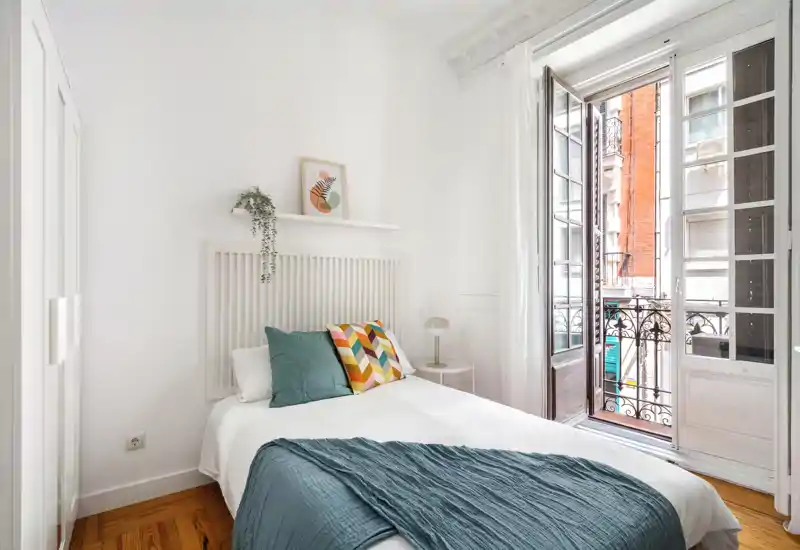 Dormitorio luminoso y con estilo con cama doble, cojines decorativos y luz natural directa desde la puerta al balcón.