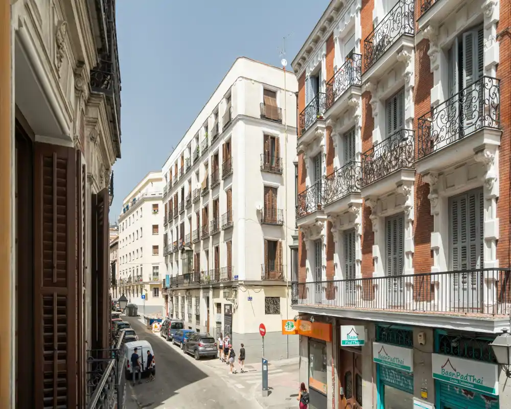 Veduta di una strada urbana soleggiata con edifici classici su più piani e negozi al piano terra, ideale per mostrare il quartiere di un appartamento in centro.