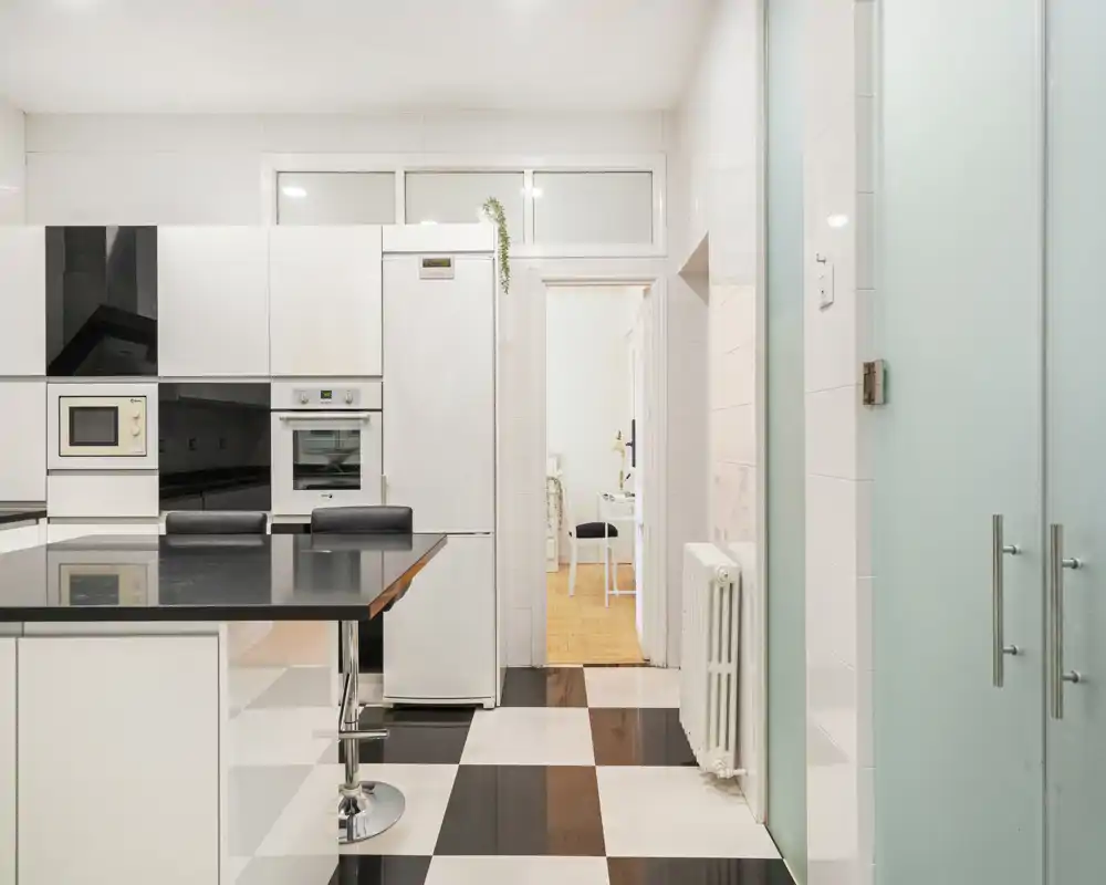 Cocina moderna y luminosa con suelo de baldosas en blanco y negro, electrodomésticos integrados y una isla con taburetes — estilo limpio y contemporáneo perfecto para anuncios.