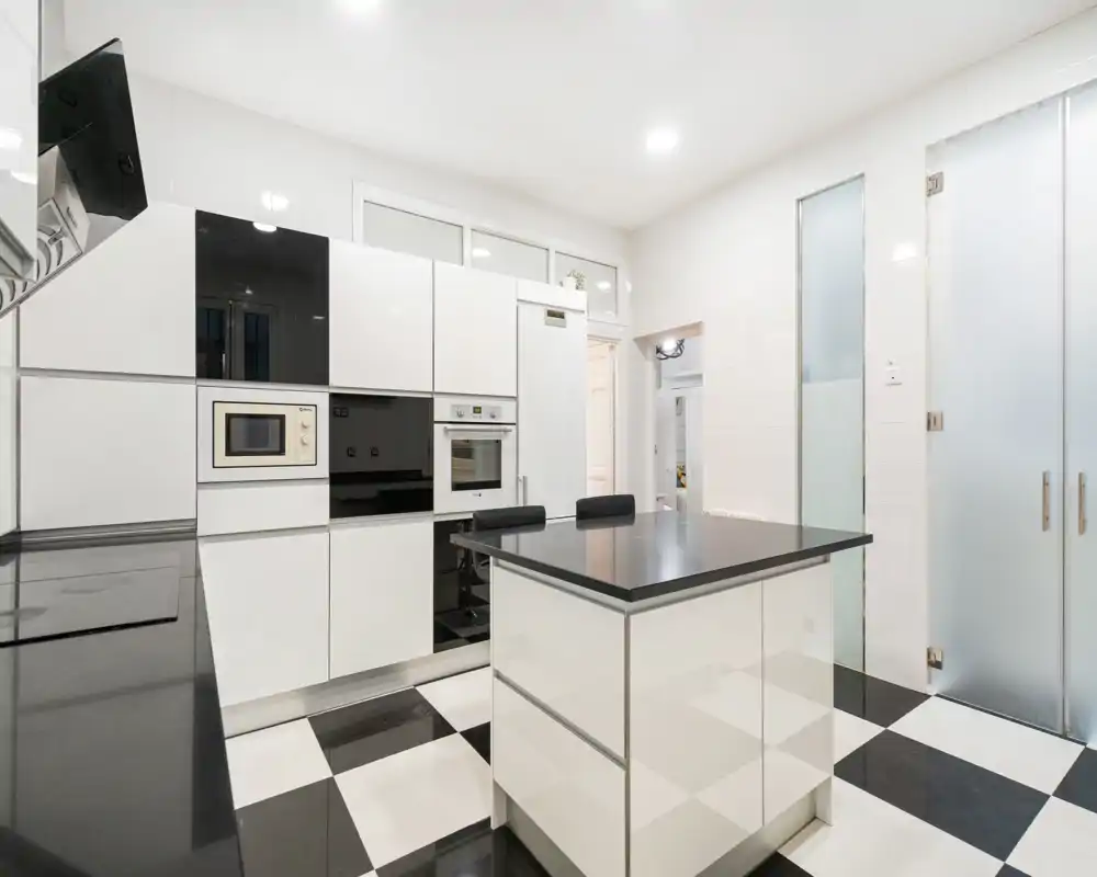 Cocina moderna y luminosa con armarios blancos brillantes, electrodomésticos integrados y una isla central con asientos — diseño limpio y contemporáneo ideal para alquileres.