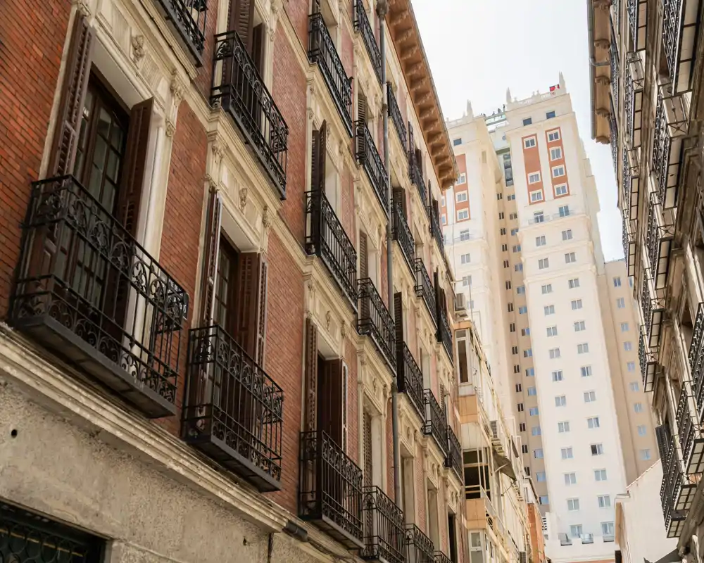 Vista exterior a nivel de calle de fachadas de edificios con balcones de hierro forjado y un edificio moderno alto al fondo; no es una habitación interior.
