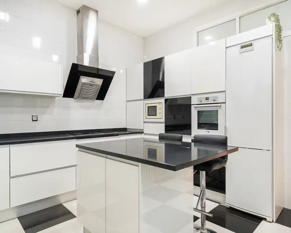 Cocina moderna y luminosa con isla central, electrodomésticos integrados y acabados brillantes en blanco y negro — ideal para anuncios de alquiler contemporáneos.
