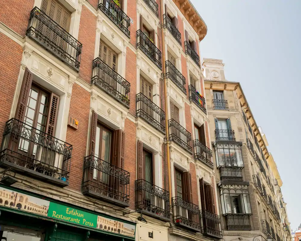 Fachada exterior de un edificio con varios balcones y persianas sobre un restaurante en planta baja — foto diurna clara que muestra detalles arquitectónicos.