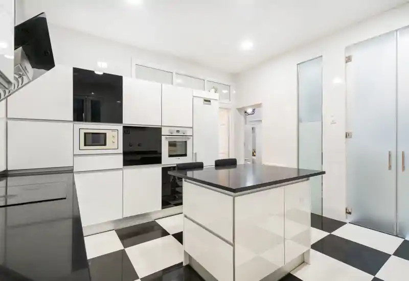 Cucina contemporanea bianca con isola centrale, elettrodomestici incassati e pavimento a scacchi bianco e nero; luminosa, elegante e ordinata per annunci.