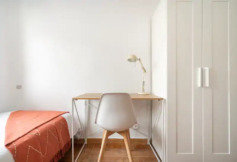 Angolo camera luminoso e minimal con letto singolo, scrivania in legno e lampada—ideale per un soggiorno compatto e accogliente con un piccolo spazio di lavoro.