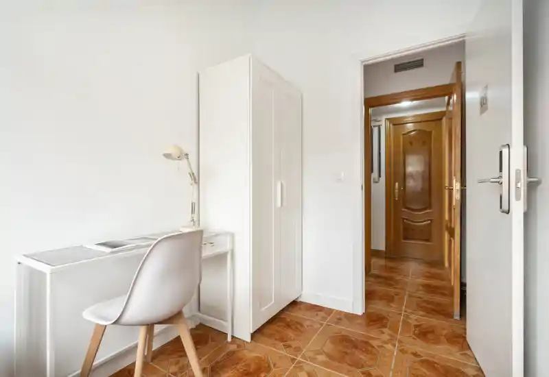 Petit coin chambre minimaliste avec une armoire blanche, un bureau compact et une chaise sur un sol carrelé — lumineux et soigné, adapté à une personne ou un coin bureau.