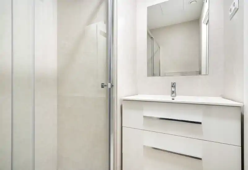 Bright, modern bathroom with a white vanity, mirror and a glass shower door; clean lines and neutral tiles create a fresh, minimalist look.