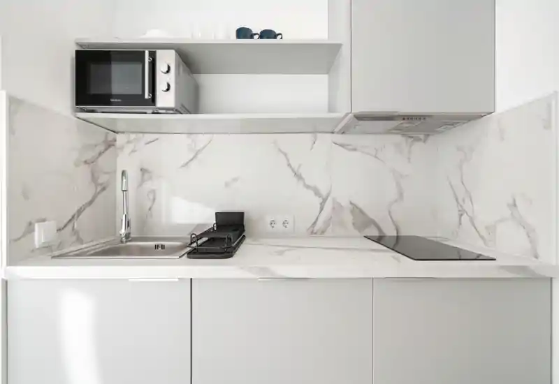 Compact modern kitchen with marble-effect backsplash, integrated induction hob, stainless sink and microwave. Clean, minimalist design ideal for short-stay rentals.