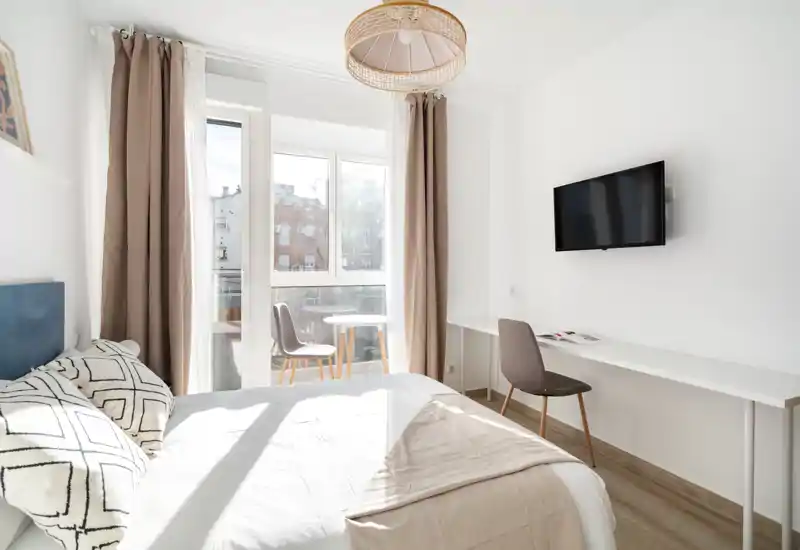 Bright, modern bedroom with a comfortable double bed facing large windows and a small desk area — ideal for relaxation and light-filled stays.