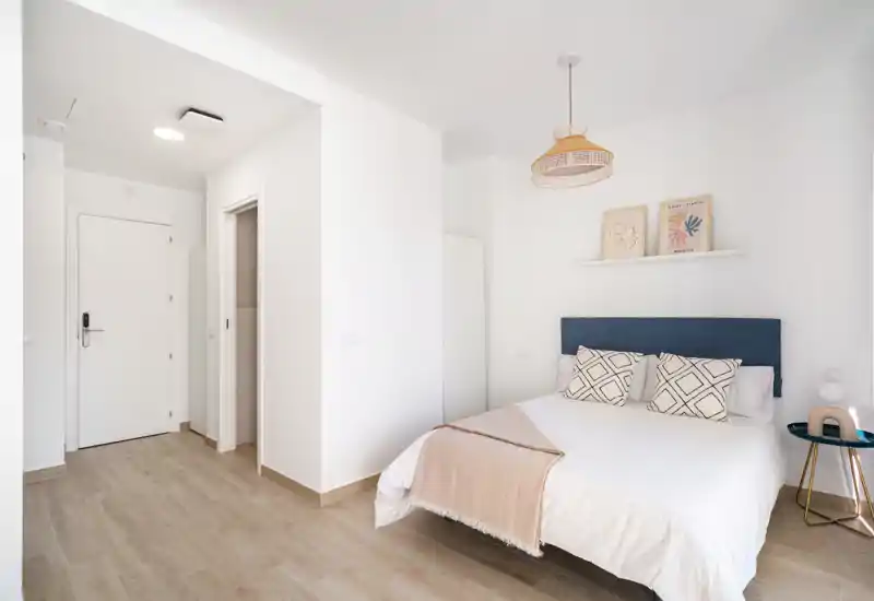 Bright, minimal bedroom with a double bed, patterned cushions and soft neutral textiles; modern, airy layout ideal for short-term rentals.