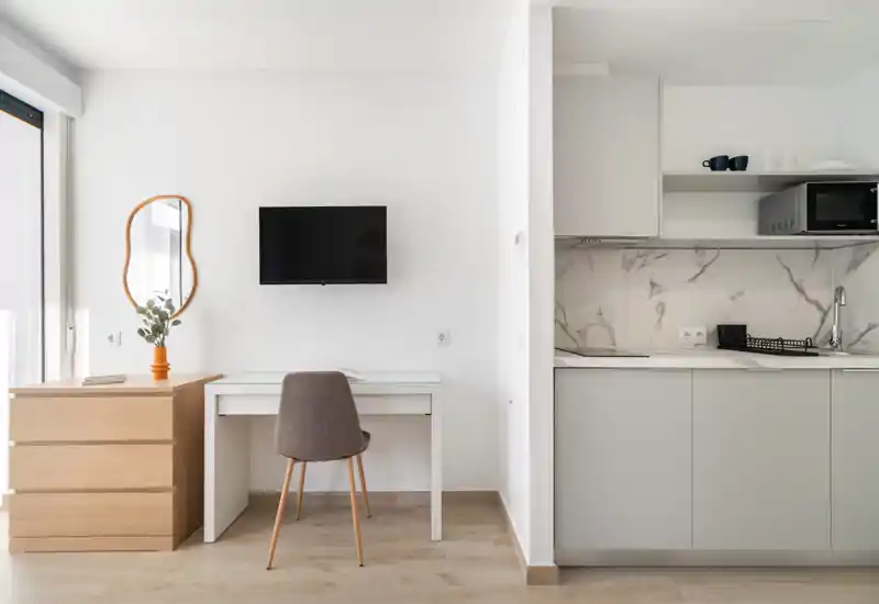 Compact modern kitchenette with marble-effect backsplash, built-in sink and microwave, paired with a small desk and chair — bright, minimal and practical for a studio stay.