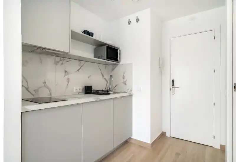 Compact modern kitchenette with grey cabinets, marble-effect backsplash, induction hob and microwave — bright, clean and space-saving for a studio.