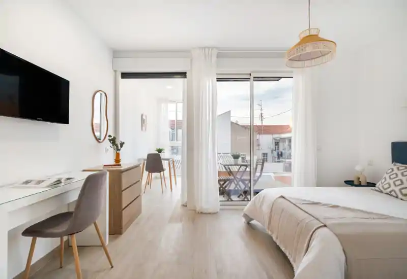 Bright, modern bedroom with a comfortable double bed, desk and balcony access. Neutral tones, natural light and simple Scandinavian-style furniture create a calm, welcoming space ideal for vacation rentals.