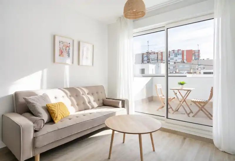 Bright, modern living room with a tufted sofa, wooden coffee table and large sliding doors opening to a sunny balcony.