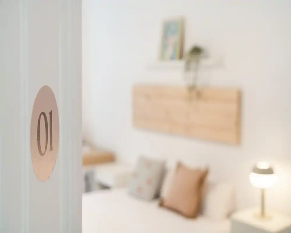 Soft-focused bedroom shot showing a bed with pillows, a bedside lamp and warm wooden accents; bright, cozy and styled for rentals.