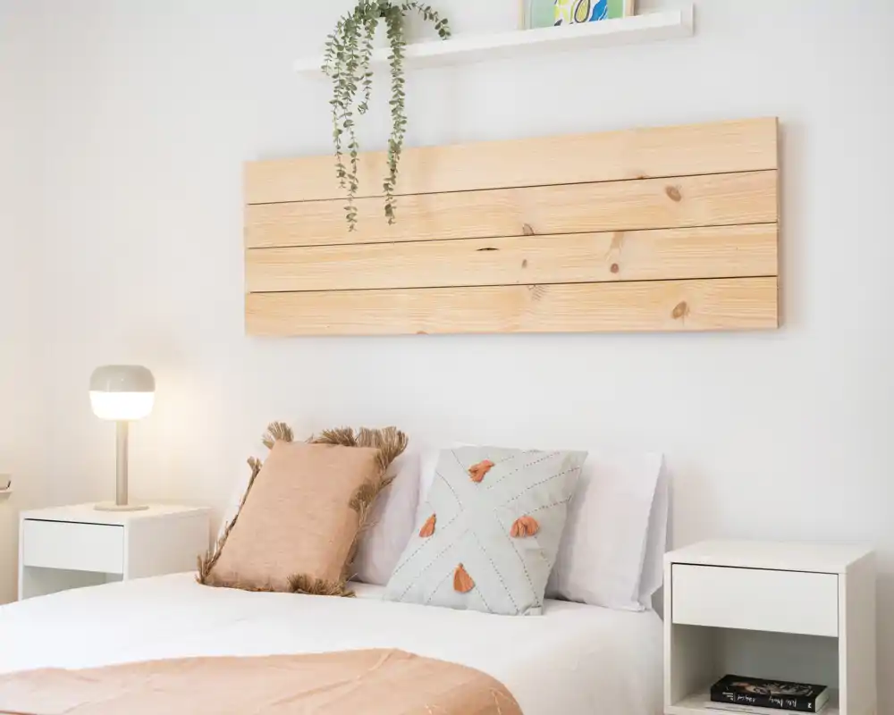 Bright, minimalist bedroom with a wooden slat headboard, decorative pillows and matching bedside tables — a calm, cozy sleeping space ideal for rental photos.