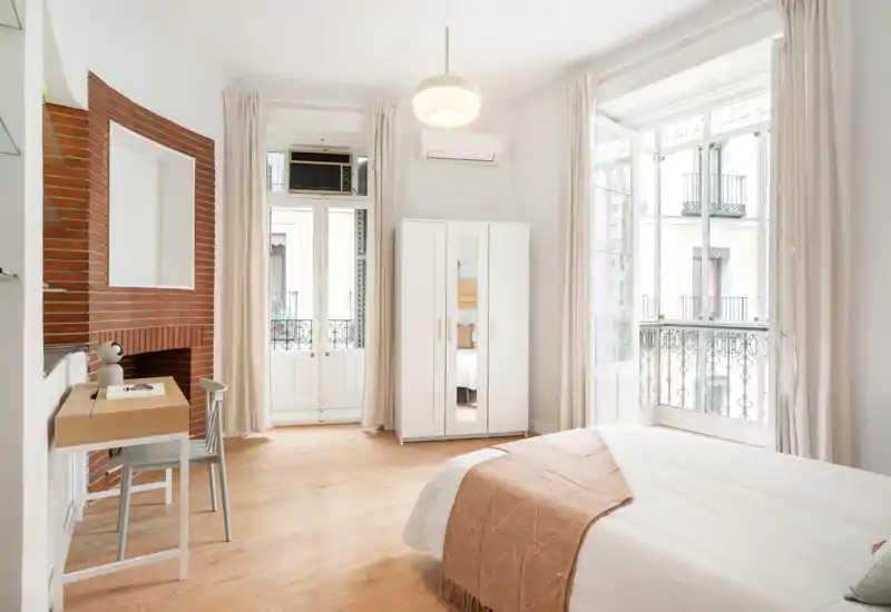 Bright, airy bedroom with a comfortable double bed, large windows and soft neutral décor creating a calm, inviting atmosphere.