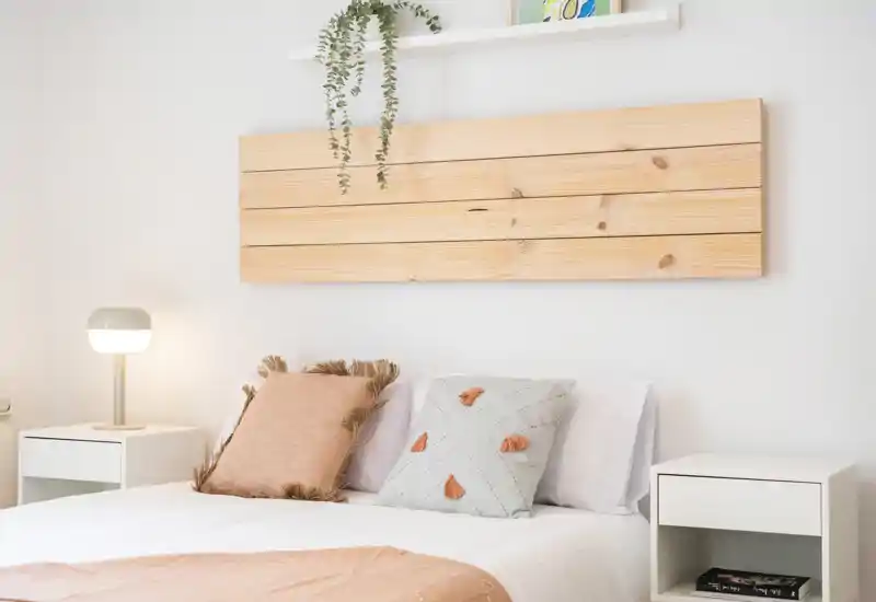 Bright, minimalist bedroom with a wooden slat headboard, decorative pillows and matching bedside tables — a calm, cozy sleeping space ideal for rental photos.