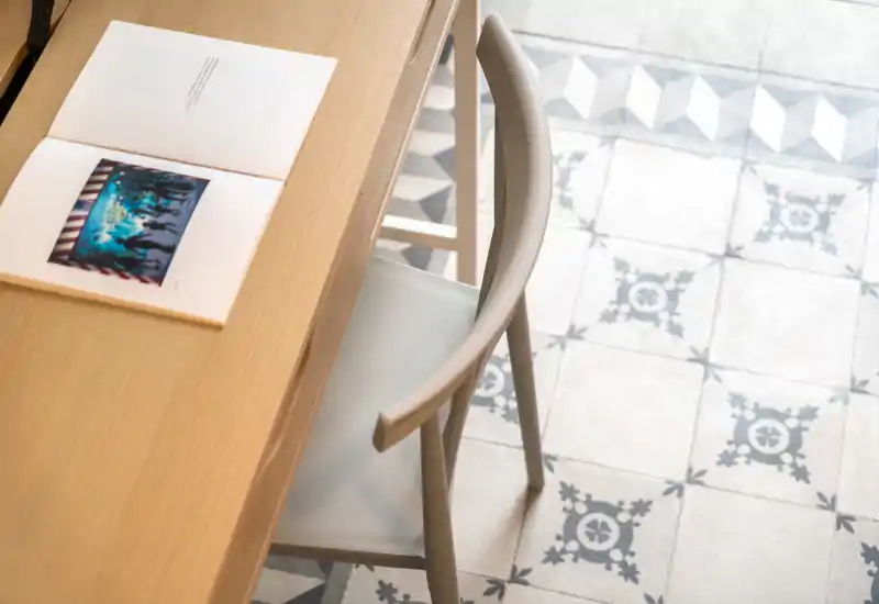 Gros plan d'un coin repas avec table en bois, chaise et sol carrelé à motifs ; une lumière naturelle douce crée une ambiance sobre et apaisante.