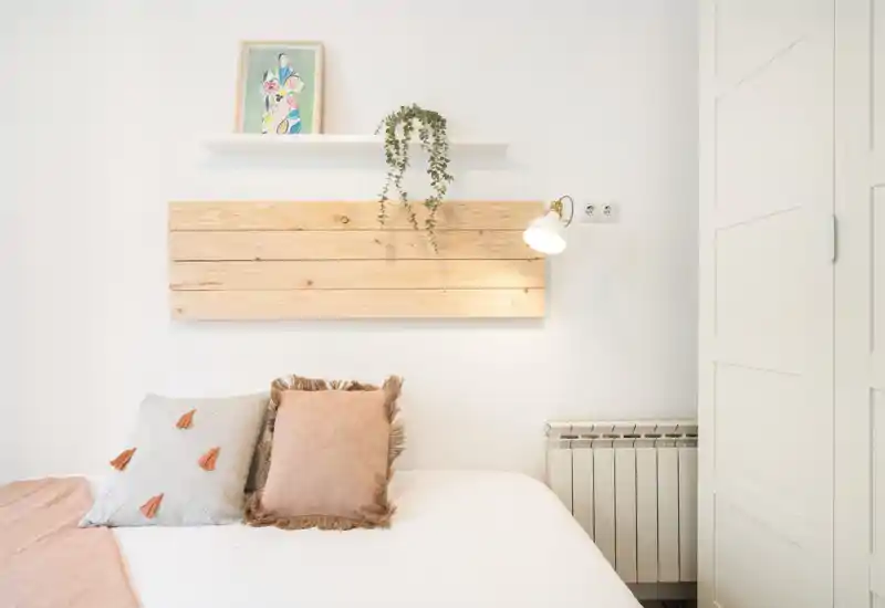 Bright, minimal bedroom with a light wooden headboard, soft textiles and decorative cushions; neutral palette creates a calm, welcoming atmosphere.