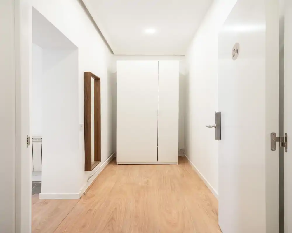 Ingresso luminoso e minimal con armadio bianco indipendente, specchio a parete e pavimento in legno chiaro — uno spazio d'arrivo pulito e moderno.