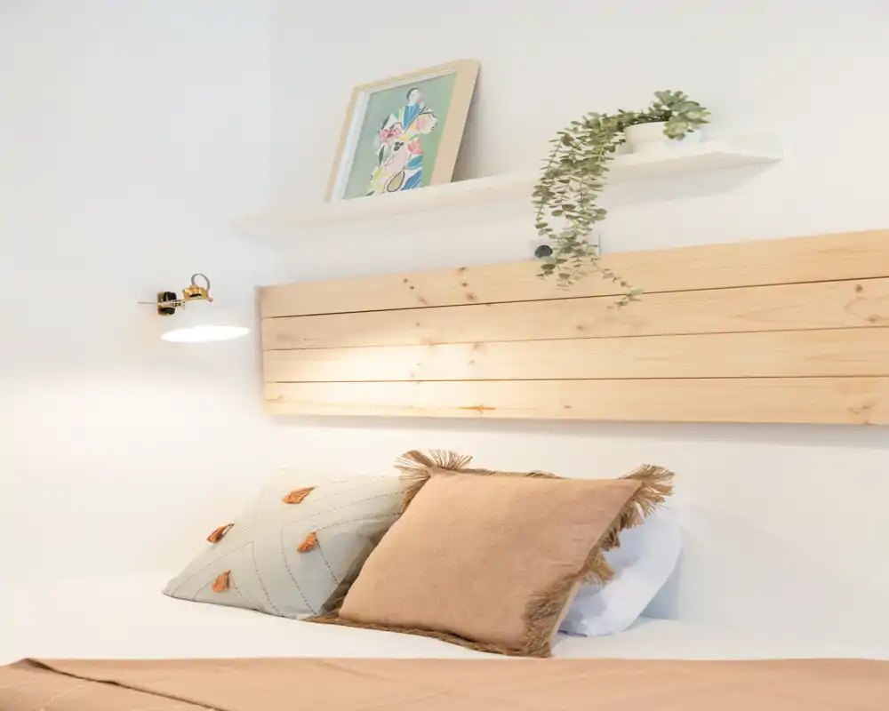 Angolo camera luminoso e accogliente con cuscini decorativi e una testiera in legno chiaro; toni neutri e una luce naturale piacevole creano un’atmosfera invitante.