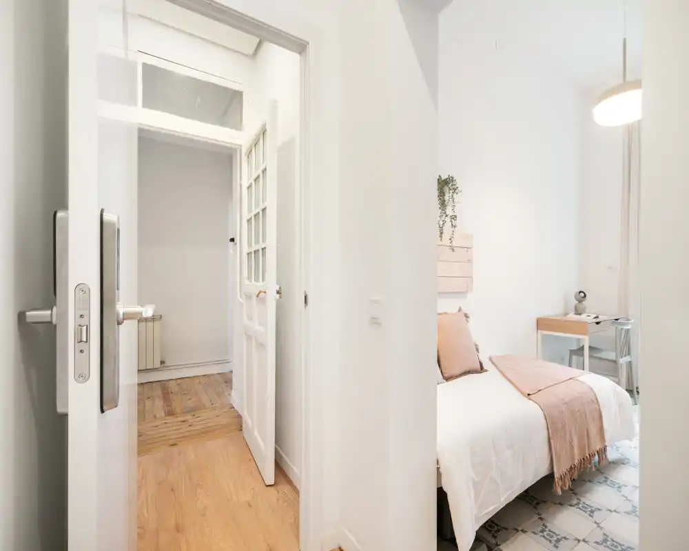 Camera da letto luminosa e minimal con letto ordinato, plaid rosa tenue e una piccola scrivania vicino alla finestra — ideale per una persona o ospiti.