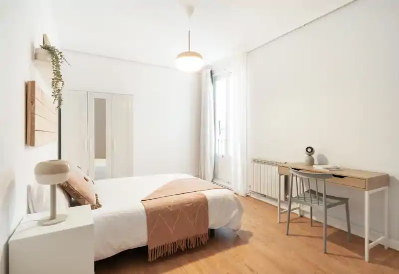 Bright, minimalist bedroom with a comfortable double bed, soft textiles and a small desk by the window — ideal for rest or remote work.