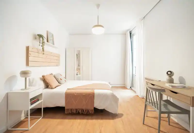 Bright, minimalist bedroom with a double bed, soft textiles and a workspace by the window — ideal for relaxed stays.