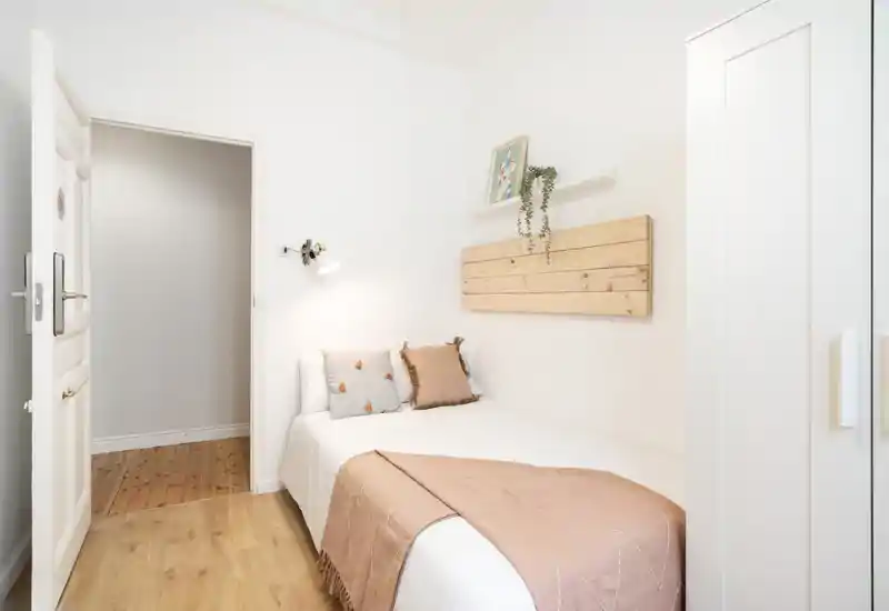 Bright, minimalist single bedroom with a neatly made bed, soft pillows and warm wooden accents. Ideal for a cozy, compact rental.