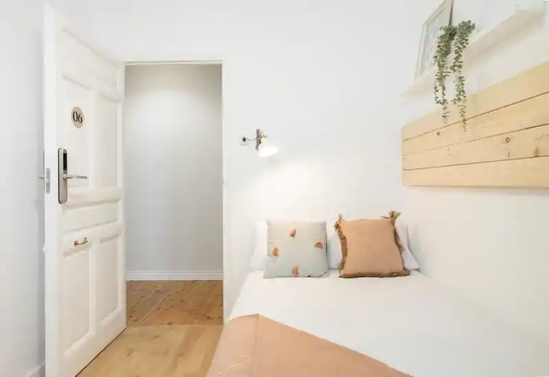 Dormitorio individual luminoso y minimalista con la cama bien hecha, cojines decorativos y detalles en madera cálida; ideal para una estancia acogedora para una persona.
