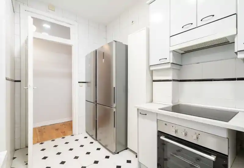 Cuisine moderne et lumineuse avec réfrigérateur en acier inox, murs carrelés et four électrique encastré avec plaque de cuisson. Agencement propre et fonctionnel, adapté aux appartements citadins.
