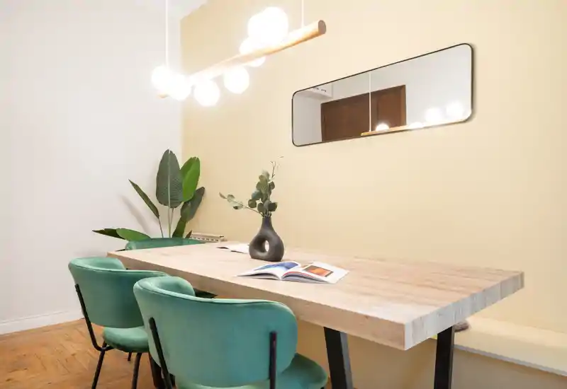 Coin repas moderne et lumineux avec table en bois massif, chaises vertes rembourrées et plantes décoratives ; idéal pour des repas détendus ou du télétravail.