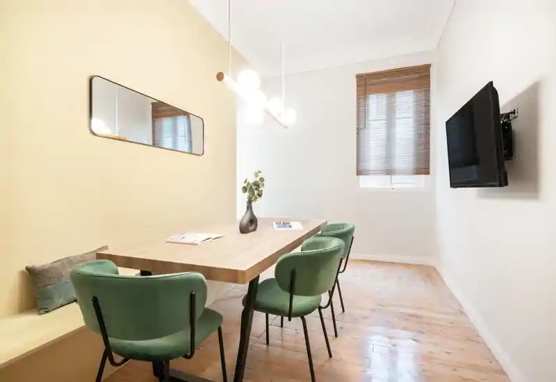 Salle à manger lumineuse et moderne avec table en bois, quatre chaises vertes rembourrées et un vase décoratif — style épuré et lumière naturelle pour un espace convivial.