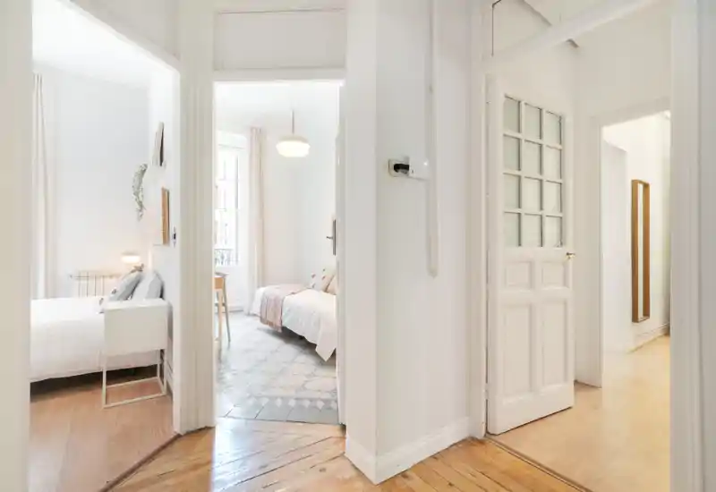 Vue lumineuse et minimaliste de chambres depuis un couloir : deux espaces de couchage adjacents avec linge de lit blanc, textiles douillets et lumière naturelle — idéale pour un annonce de location.