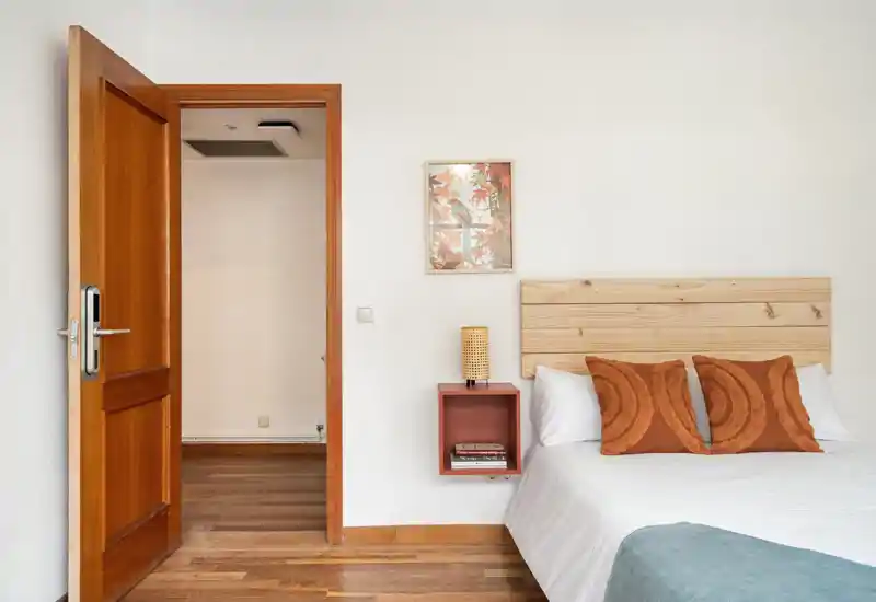 Bright, warmly styled bedroom with a wooden headboard, decorative pillows and a neat white bedspread — ideal for a cozy night's rest.