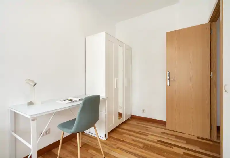 Petite pièce lumineuse avec une armoire blanche et un bureau minimaliste avec chaise — idéale comme petite chambre ou coin bureau. Sol en bois et murs neutres pour un rendu épuré.