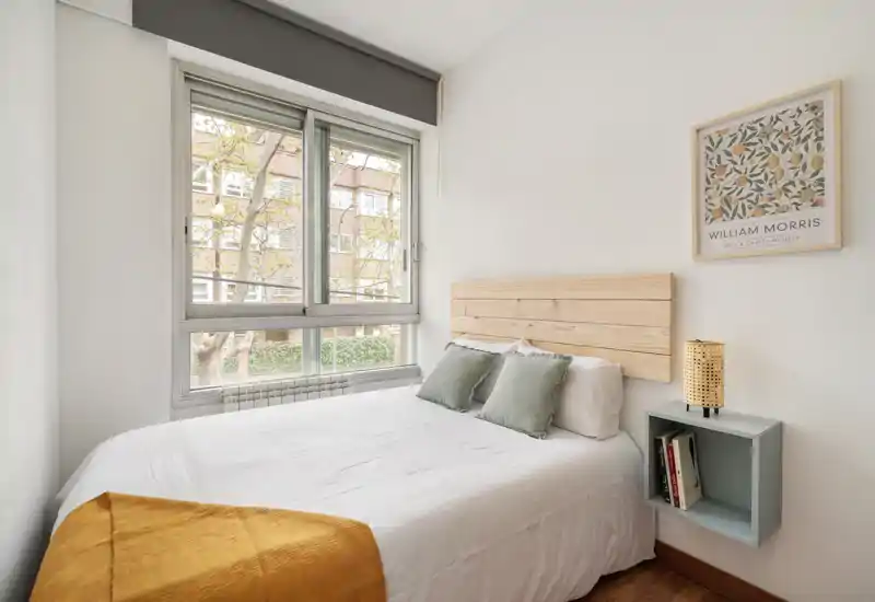 Dormitorio luminoso y bien decorado con cama doble, cabecero de madera, cojines decorativos y gran ventana que aporta luz natural — ideal para anuncios.