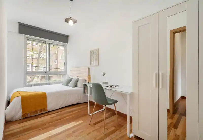 Habitación individual luminosa y moderna con cama cómoda, suelos de madera y zona de estudio junto a la ventana—ideal para estudiante o profesional.