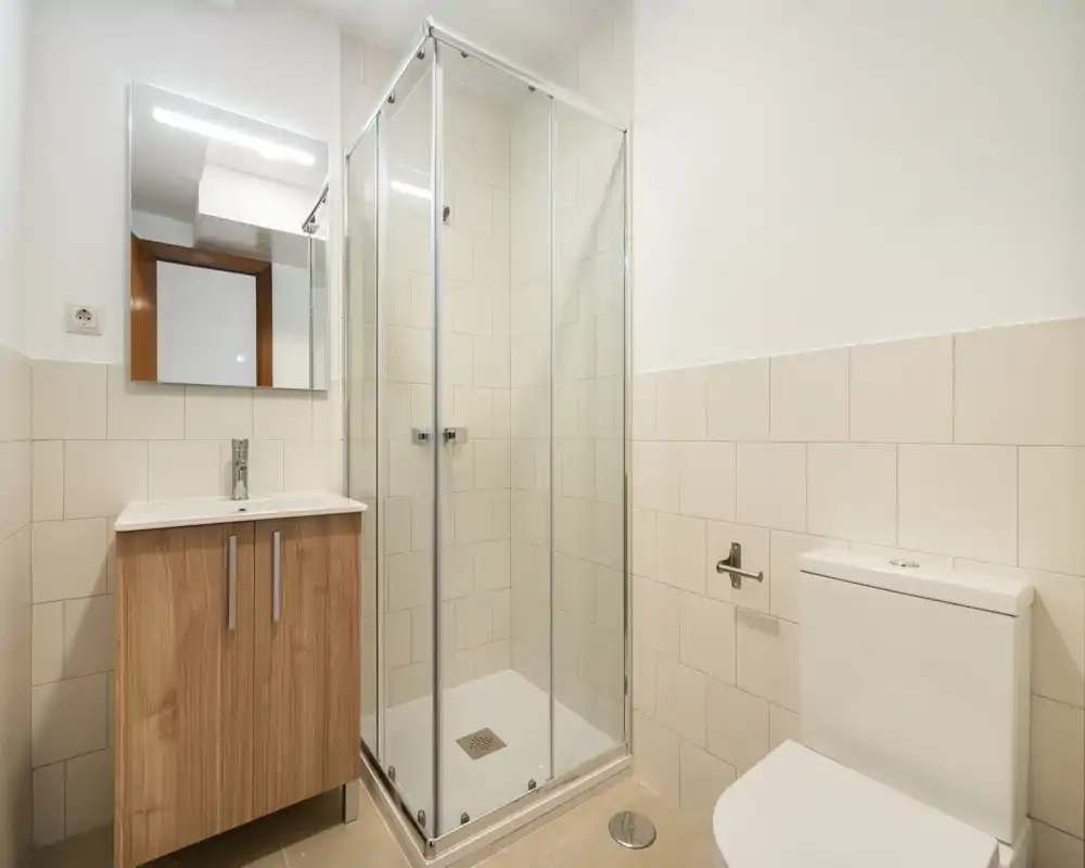 Bagno moderno e luminoso con cabina doccia in vetro, mobile lavabo con specchio e wc. Piastrelle neutre e linee pulite per uno spazio funzionale e fresco.