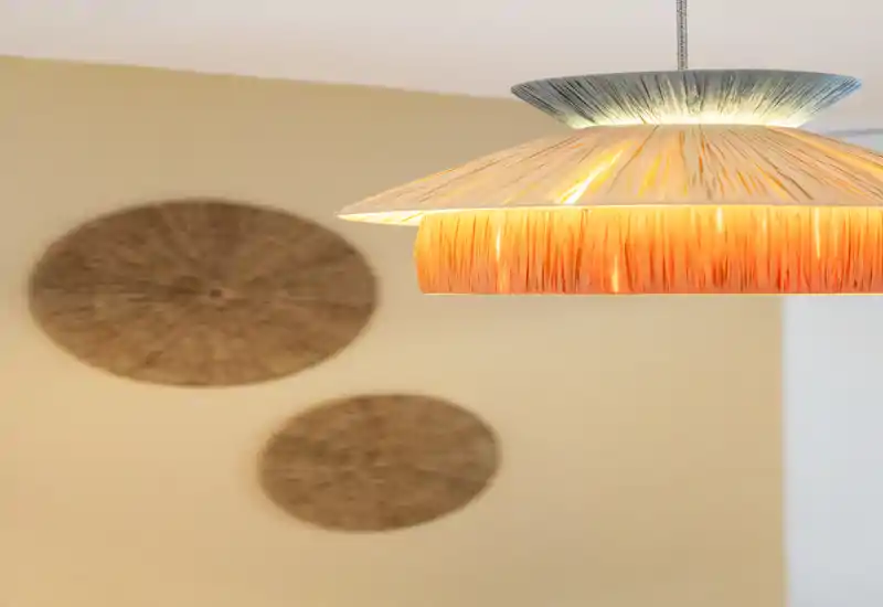 Gros plan chaleureux d'un luminaire suspendu avec des éléments décoratifs en osier en arrière‑plan flou, créant une ambiance de salon cosy.