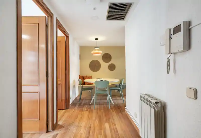 Coin repas chaleureux avec une table ronde, des chaises vert menthe et un éclairage suspendu chaleureux; parquet et décors muraux créent une ambiance accueillante.