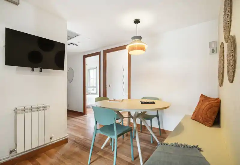 Coin repas chaleureux avec table ronde, quatre chaises et banquette, parquet et suspension lumineuse—idéal pour petits repas et réunions conviviales.